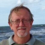 Colour head and shoulders photograph of Timothy Dowse, with the sea behind him