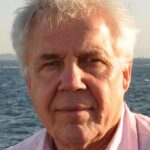 Colour head and shoulders photograph of Ian Whitting, with the sea behind him