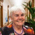 Colour head and shoulders photo of Vivien Life, wearing a dark flowered top and purple necklace