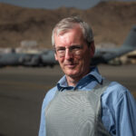 Colour photo of Sir Laurie Bristow in front of a plane at Afghanistan airport